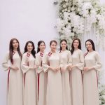 Nhóm các cô gái mặc áo dài trắng ngà phối đỏ thanh lịch trong studio với hoa trắng.