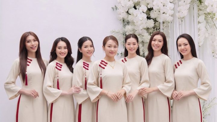 Nhóm các cô gái mặc áo dài trắng ngà phối đỏ thanh lịch trong studio với hoa trắng.
