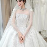 Một cô dâu xinh đẹp mặc váy cưới trắng đính đá sang trọng trong studio.