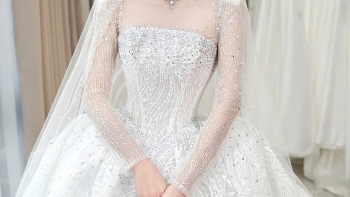 Một cô dâu xinh đẹp mặc váy cưới trắng đính đá sang trọng trong studio.