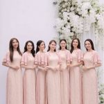 Nhóm các cô gái mặc áo dài màu hồng pastel thanh lịch trong studio với decor hoa trắng.