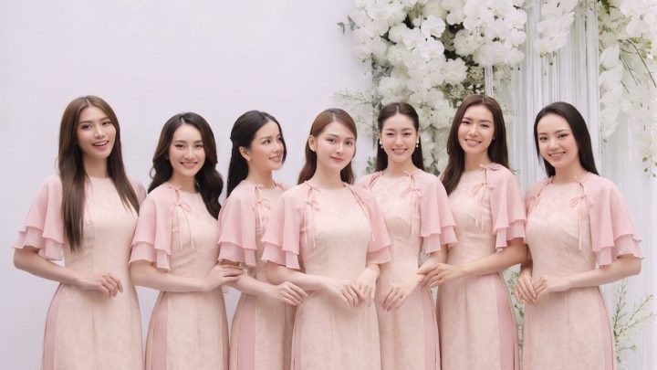 Nhóm các cô gái mặc áo dài màu hồng pastel thanh lịch trong studio với decor hoa trắng.