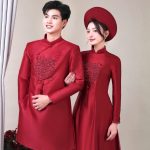 Một cặp đôi mặc áo dài truyền thống màu đỏ chụp trong không gian studio sang trọng.
