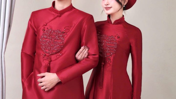 Một cặp đôi mặc áo dài truyền thống màu đỏ chụp trong không gian studio sang trọng.