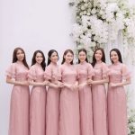 Nhóm các cô gái mặc áo dài hồng pastel chụp tại studio với hoa trắng.