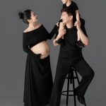 Ảnh chụp gia đình gồm bố, mẹ bầu và con trai trong trang phục màu đen trên nền studio xám.