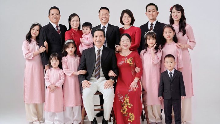 Ảnh chụp gia đình nhiều thế hệ mặc áo dài và vest trong studio với phông nền trắng.