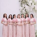 Nhóm các cô gái mặc áo dài hồng pastel chụp tại studio với hoa trắng.