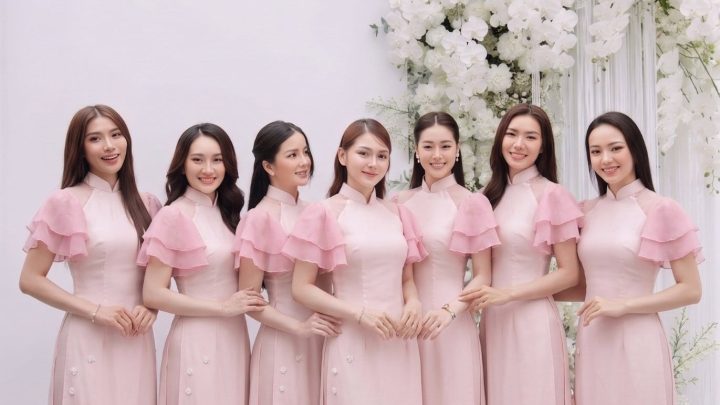 Nhóm các cô gái mặc áo dài hồng pastel chụp tại studio với hoa trắng.