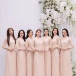 Nhóm các cô gái mặc áo dài màu hồng pastel thanh lịch trong studio với decor hoa trắng.